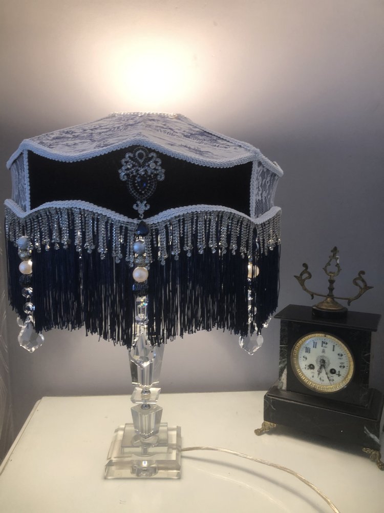 victorian_fringed_lampshade, in blue velvet toile and lace, with diamantes and blue fringe on a  glass lamp  next  to an antique clock. 
